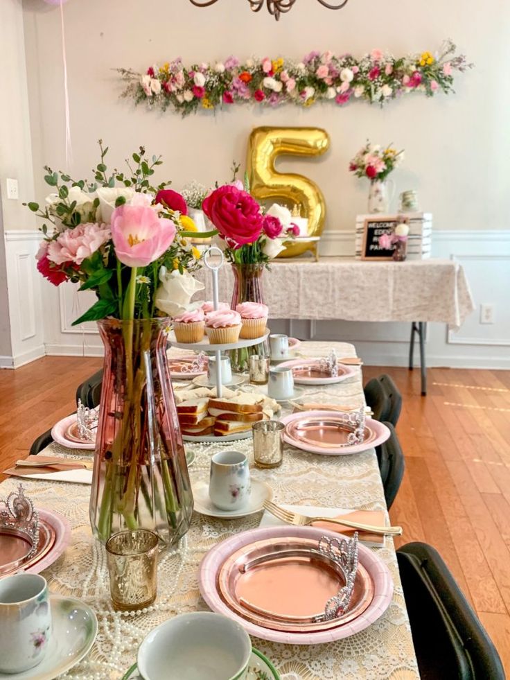 the table is set with pink and white flowers in vases, plates, cups, and saucers