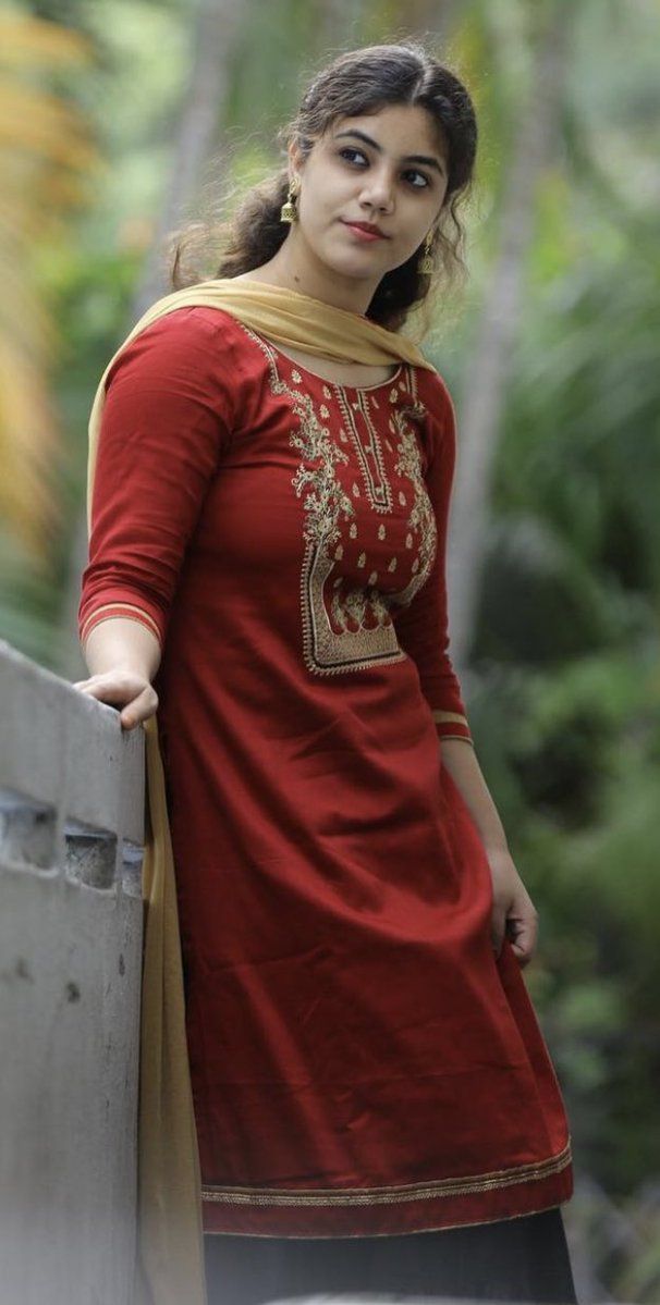 a woman in a red and gold dress leaning against a wall with her hand on the side