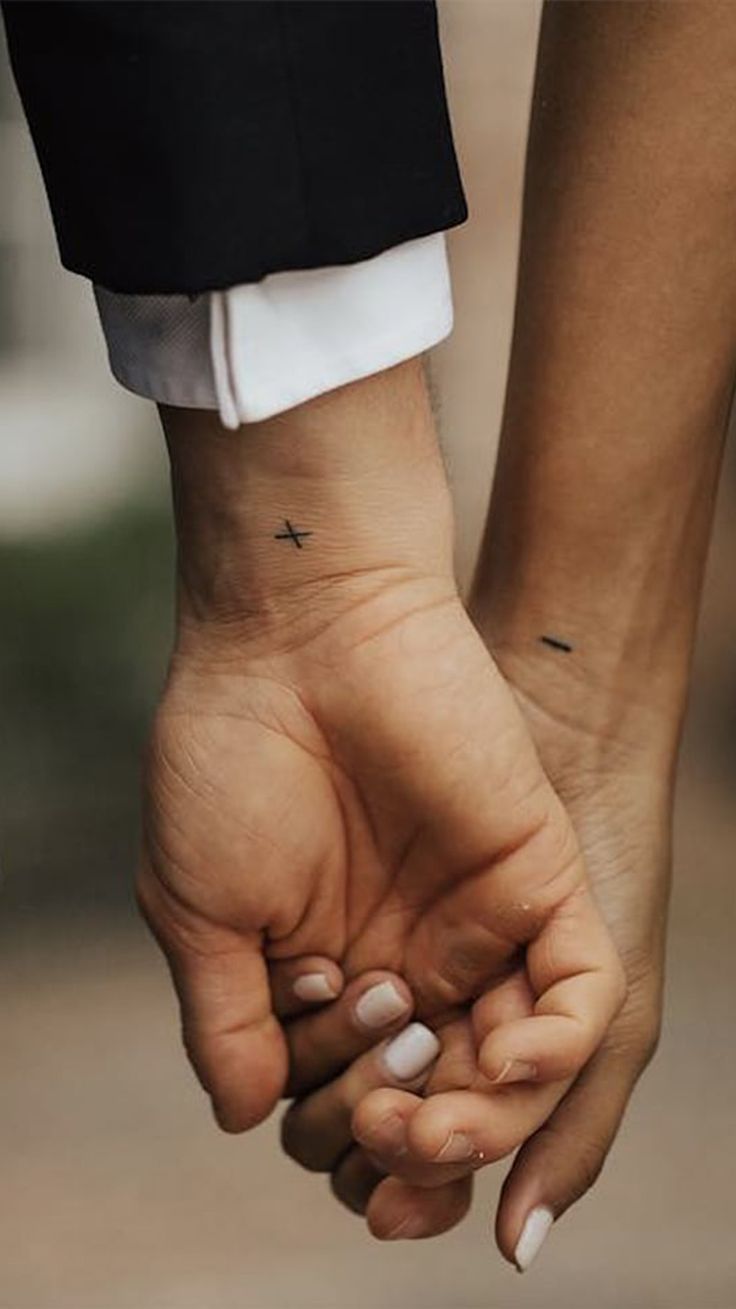 two people holding hands with small crosses on their wrist tattooing each other's fingers