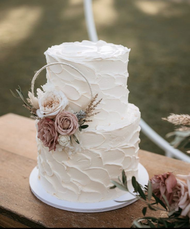 a wedding cake sitting on top of a wooden table next to pink flowers and greenery