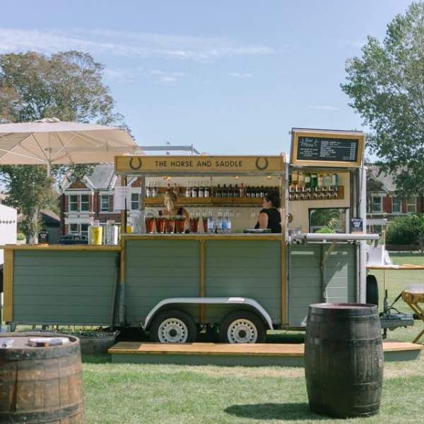 a food truck is parked in the grass near some barrels and tables with umbrellas