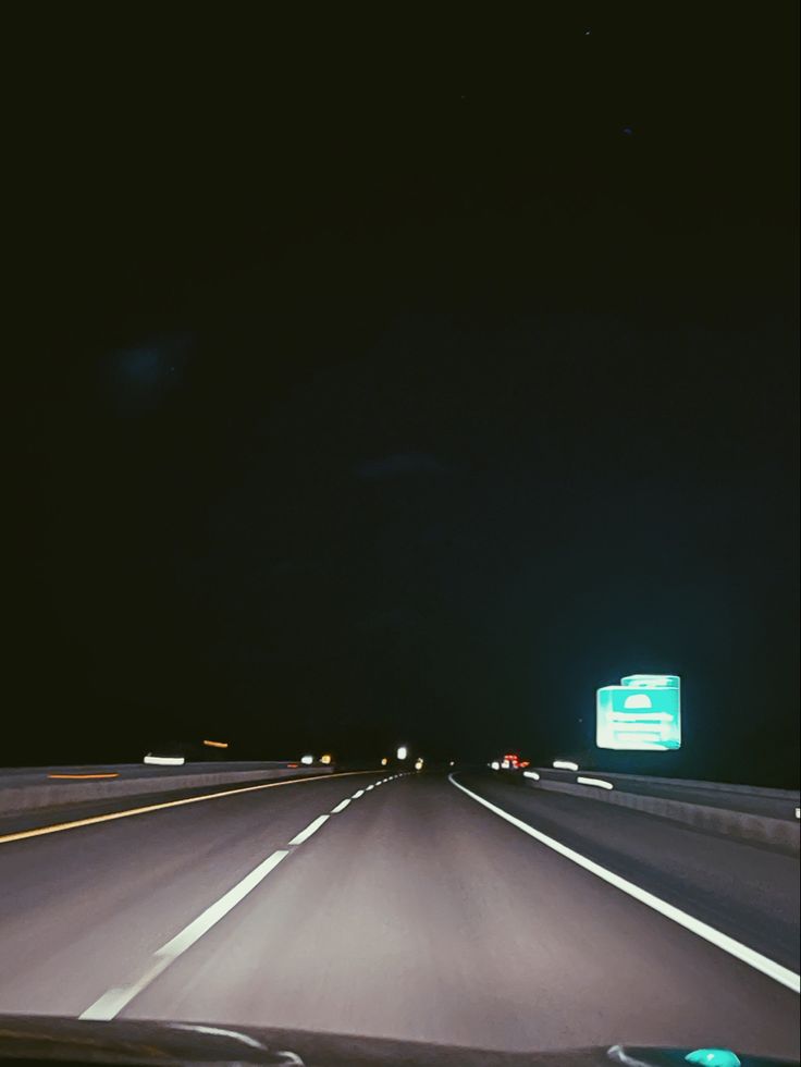 an empty highway at night with the lights on and signs in the dark behind it