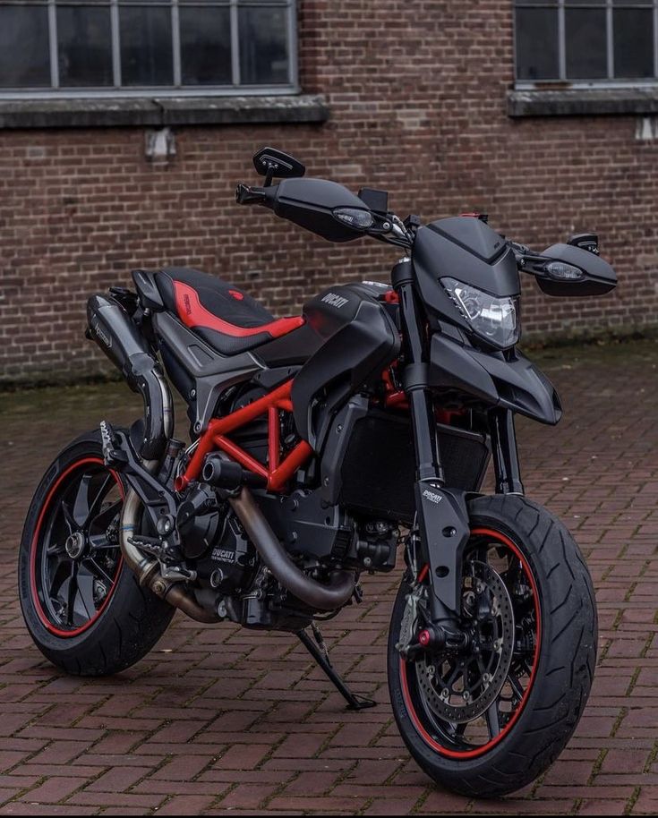 a black and red motorcycle parked on top of a brick road next to a building