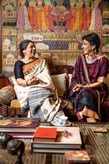 two women sitting next to each other in front of a wall with paintings on it