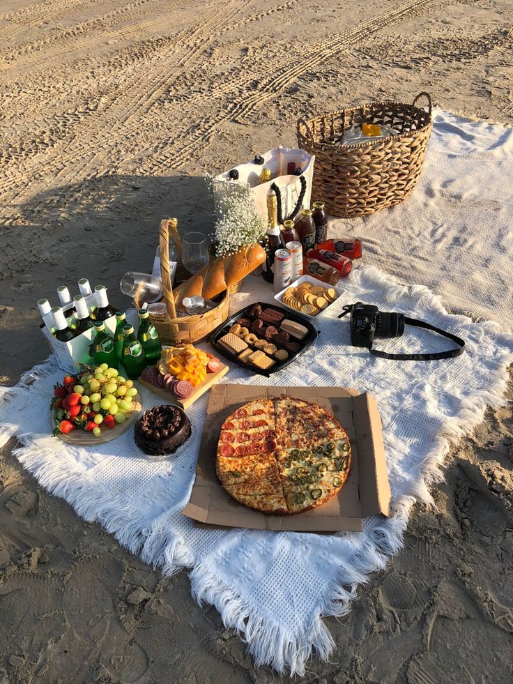 a pizza sitting on top of a sandy beach next to a picnic table filled with food