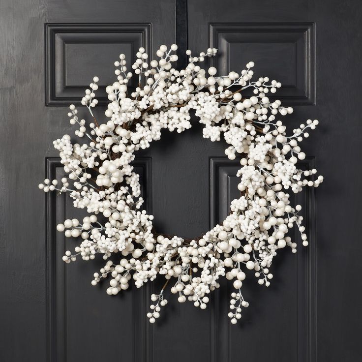 a wreath with white flowers hanging on a black front door, decorated with branches and berries