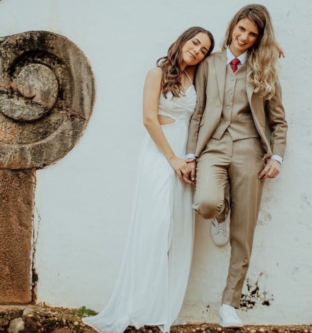 a man and woman standing next to each other in front of a white wall wearing wedding attire