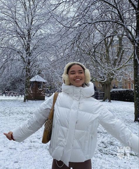 a woman standing in the snow wearing a white coat and fur - lined hat with her arms outstretched