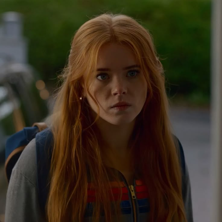 a woman with long red hair is looking at the camera while standing in front of a car