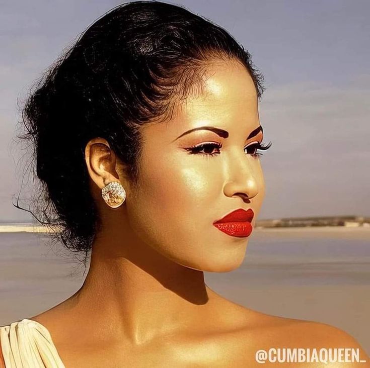 a woman with red lipstick and earrings on the beach