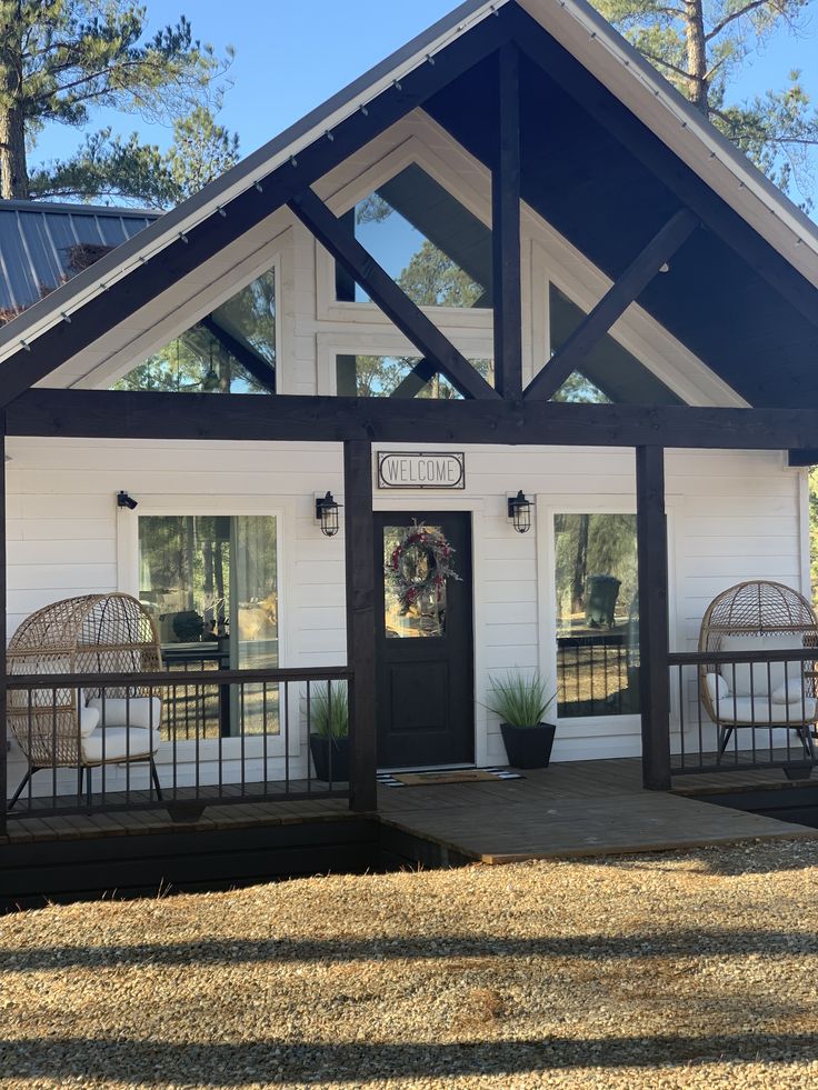 a small white house with a black front door and two wicker chairs on the porch