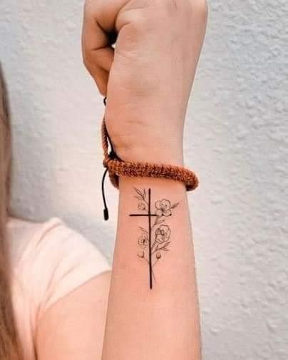 a woman's arm with a cross and flowers tattoo on her left wrist, next to a white wall