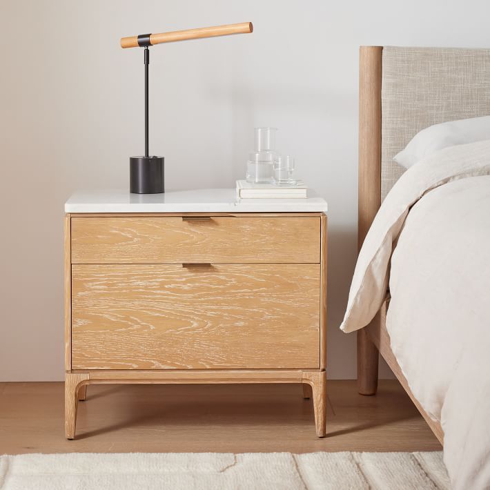 a bedroom with a bed, nightstand and lamp on top of the night stand in front of the bed