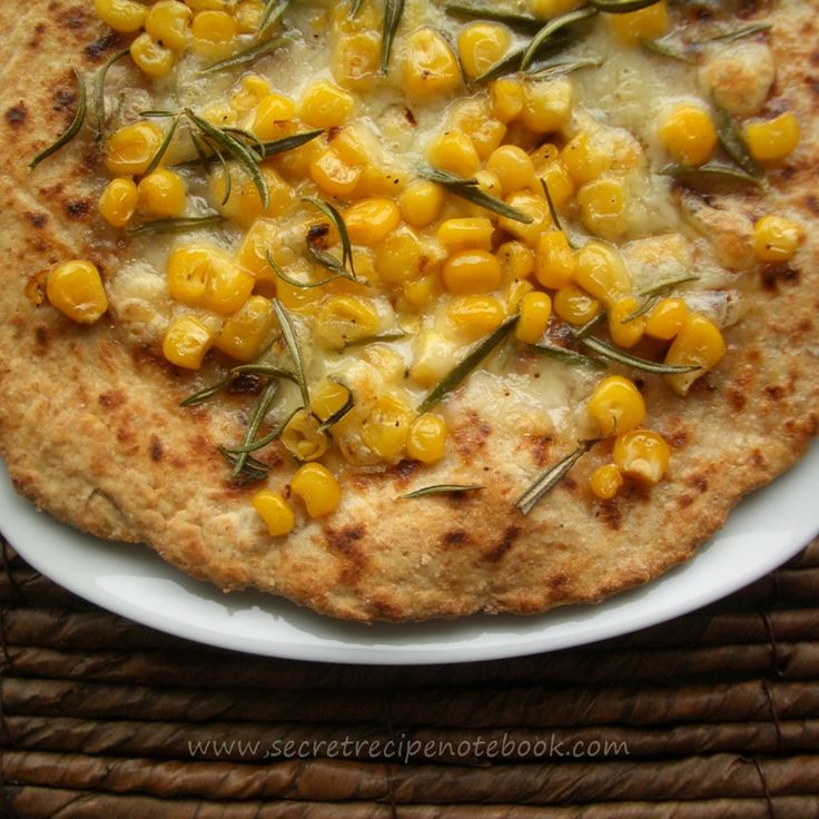 a pizza with corn on it sitting on top of a white plate next to a bamboo mat