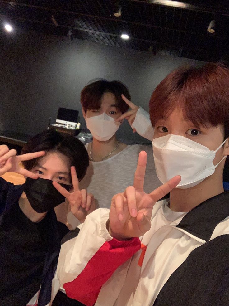 three people wearing face masks and making the peace sign with their hands in front of them