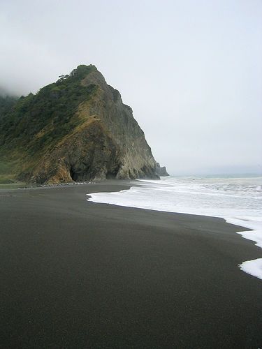 a black sand beach with waves coming in to the shore and a rock outcropping