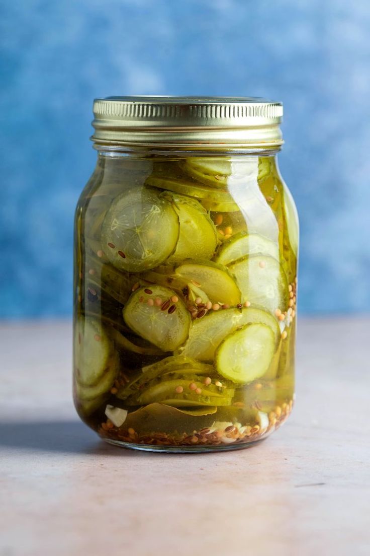 a jar filled with pickles sitting on top of a wooden table next to a blue wall