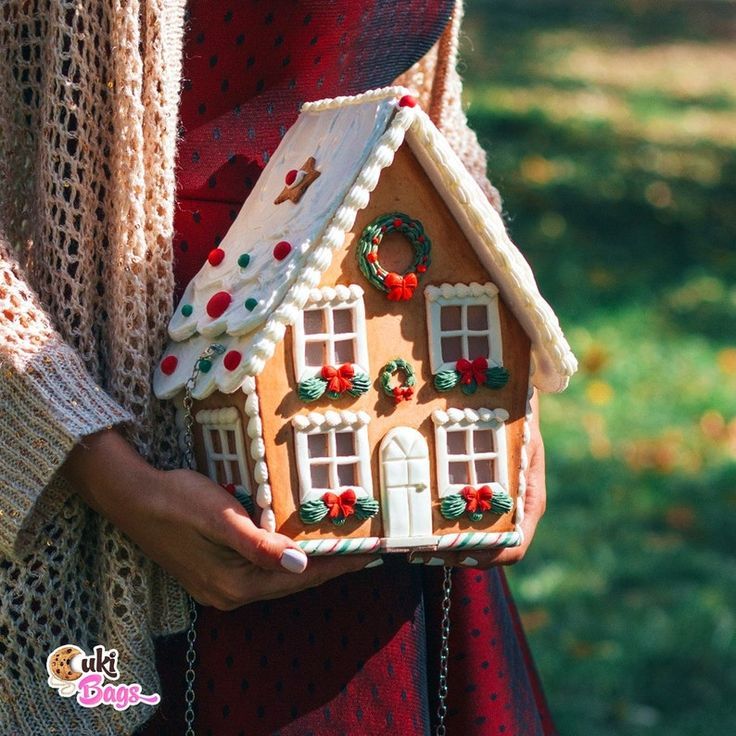 a woman is holding a gingerbread house