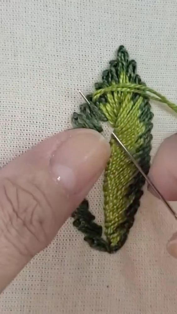 someone is stitching something green on a piece of cloth