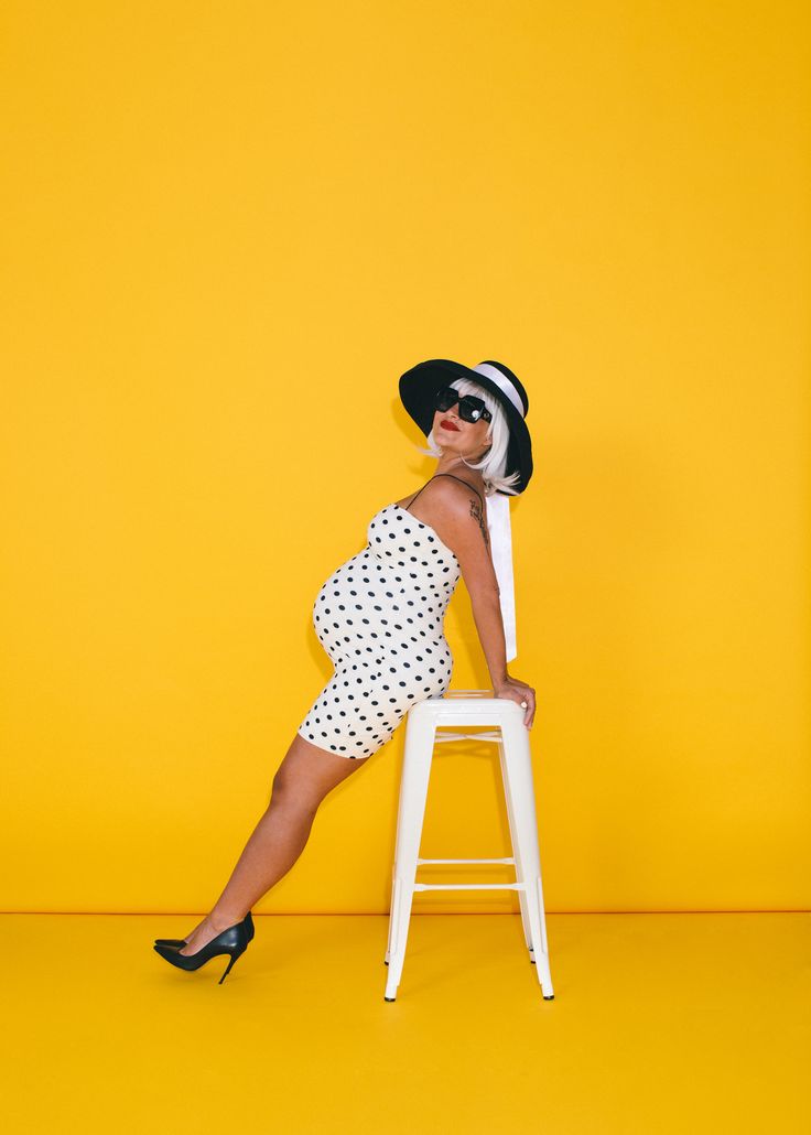 a woman sitting on top of a white chair in front of a yellow wall wearing a black and white hat