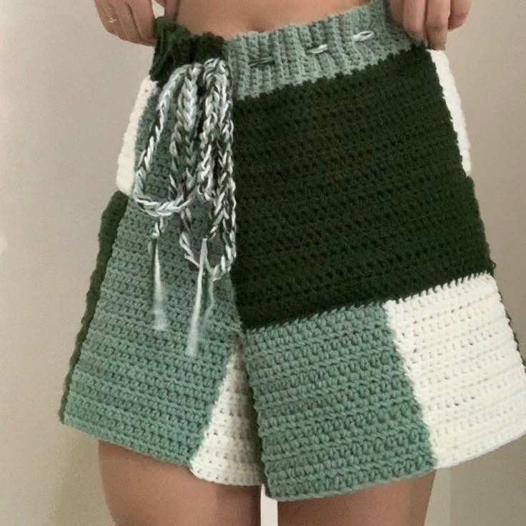 a woman is holding onto her green and white crocheted shorts