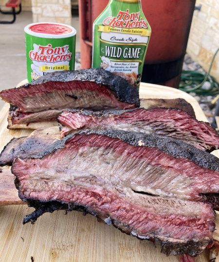 some meat is sitting on a cutting board next to two cans of hot sauces