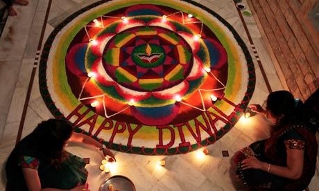 two women sitting on the floor in front of a happy diwal sign with lights