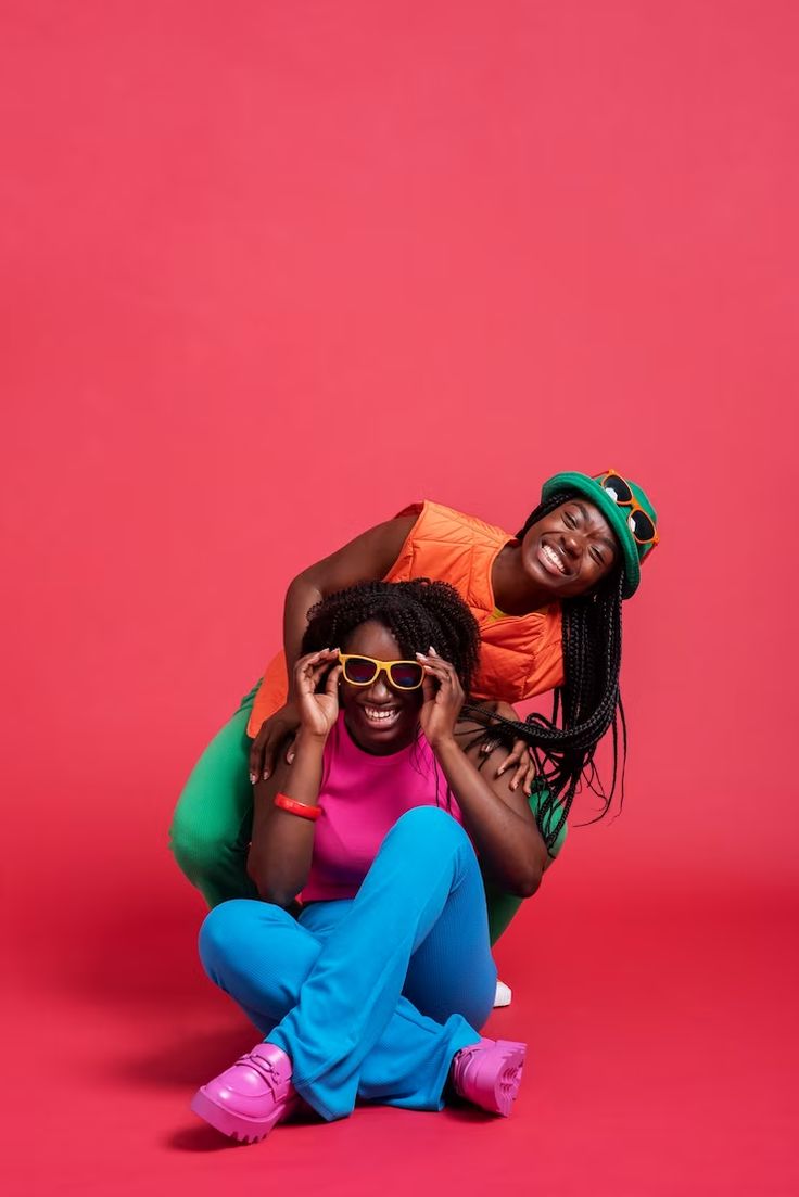 two women sitting on the ground with their arms around each other and one holding her head