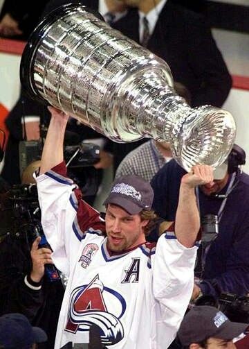 a hockey player holding up the stanley cup in front of his head and people behind him