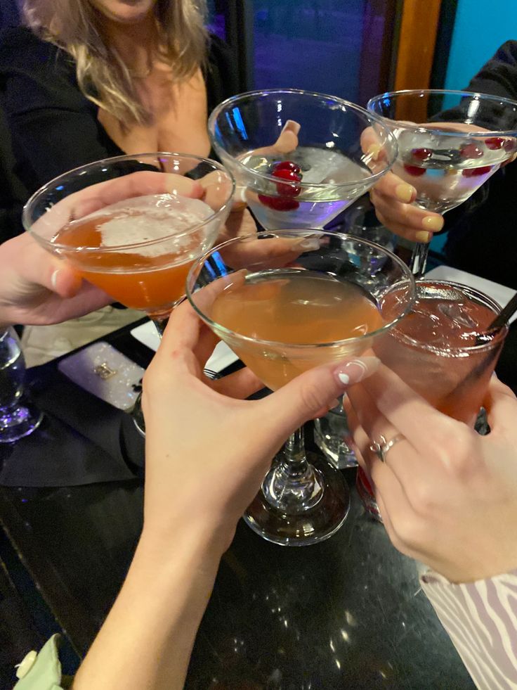 several people holding up wine glasses filled with different types of drinks on a bar top