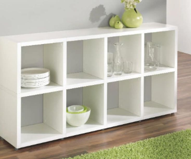 a white shelf with plates and bowls on top of it in a room next to a green rug