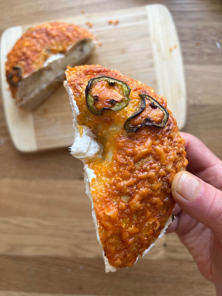 someone holding up a piece of pizza on a cutting board