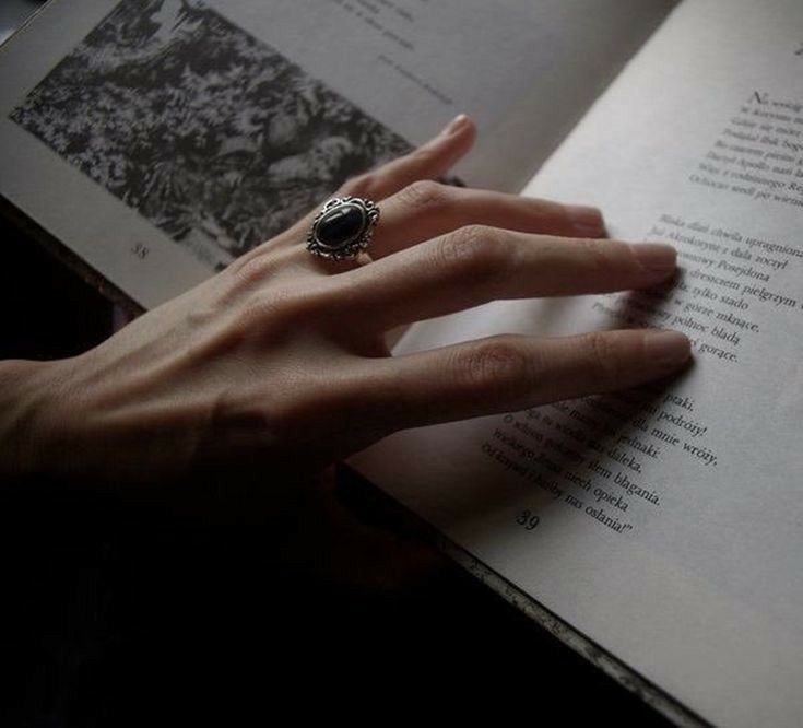 a woman's hand is holding an open book with a ring on it,