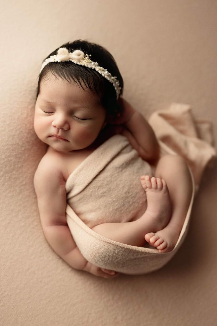 a baby is sleeping in a blanket on top of the floor wearing a headband