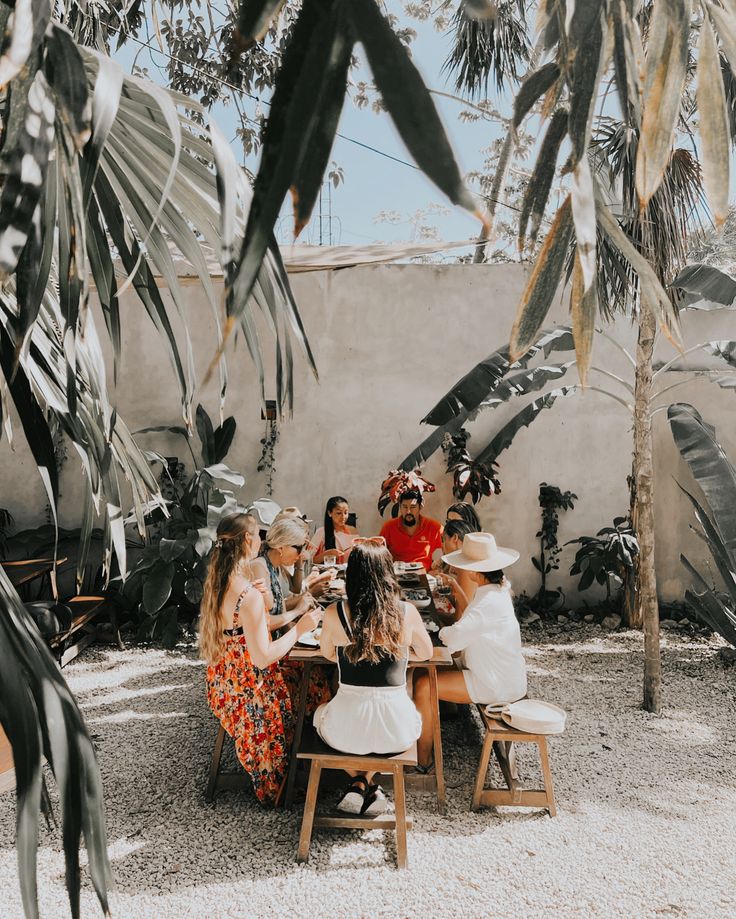 people sitting at a table in the middle of a courtyard with palm trees around them