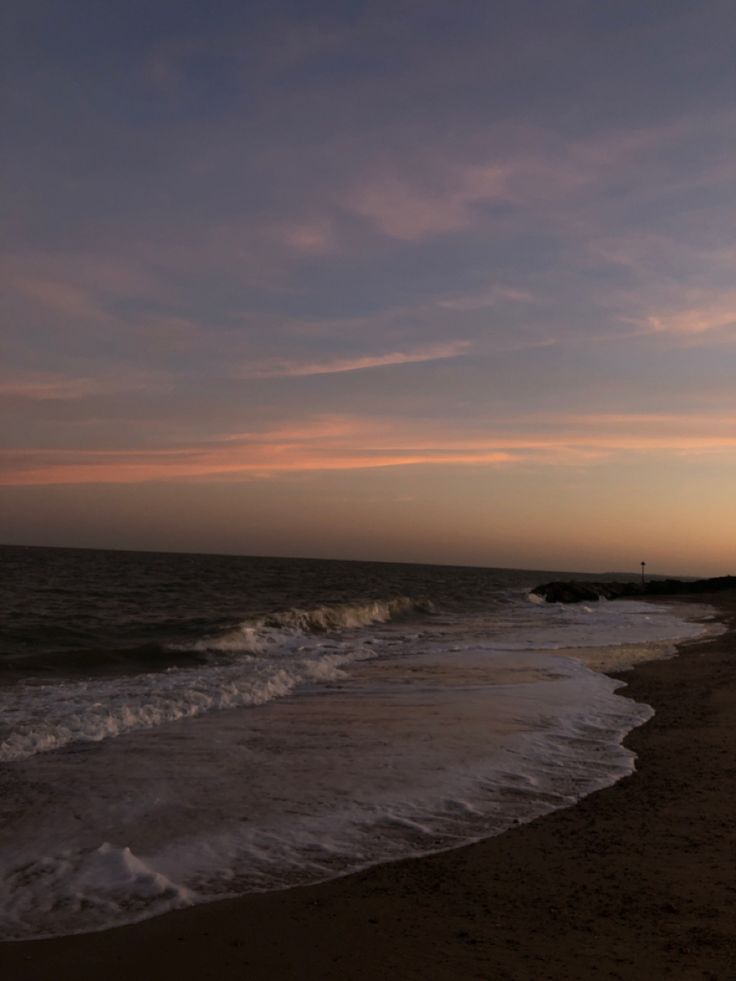 the sun is setting at the beach with waves coming in