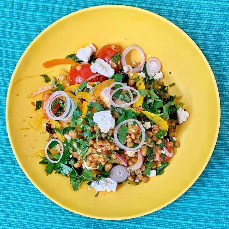 a yellow plate filled with vegetables and meat on top of a blue table cloth next to a fork