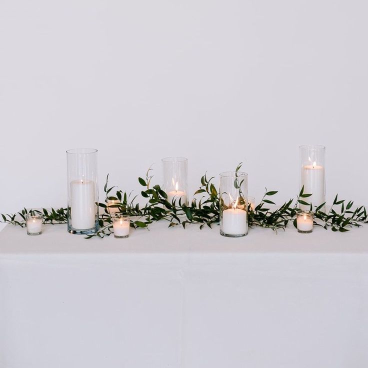 candles are lined up on a table with greenery