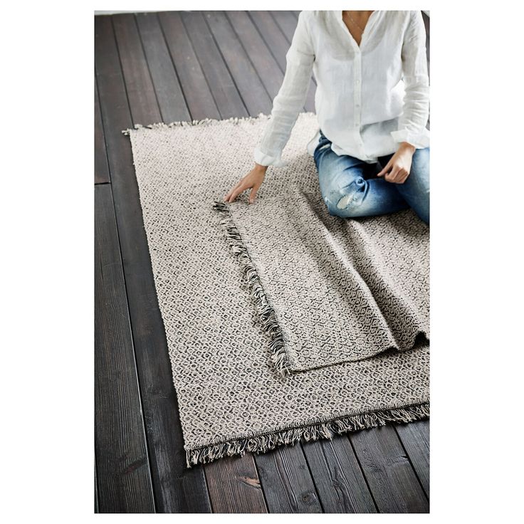 a woman sitting on top of a wooden floor next to a rug with fringes