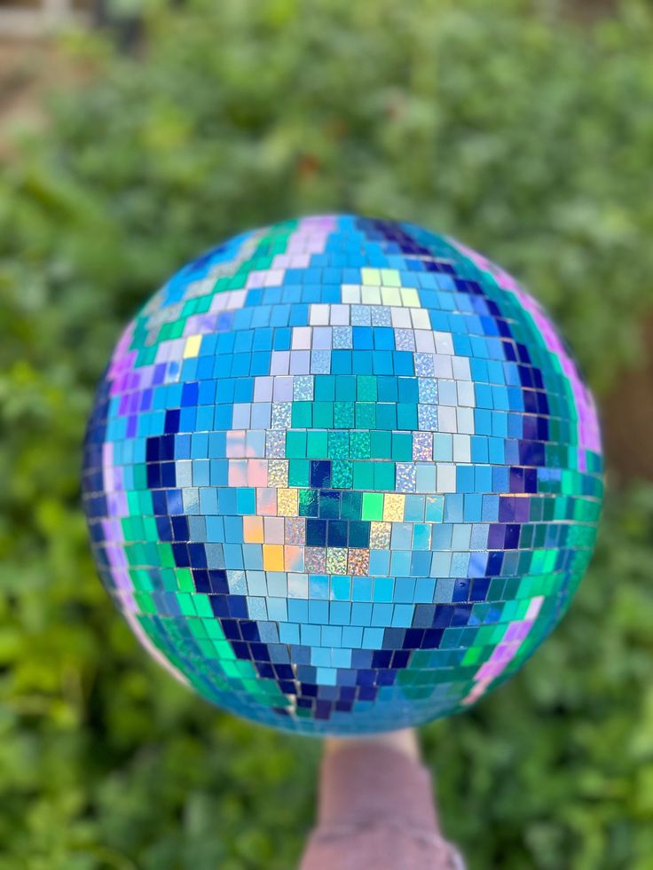 a blue and green mosaic ball sitting on top of a wooden stick in front of some bushes