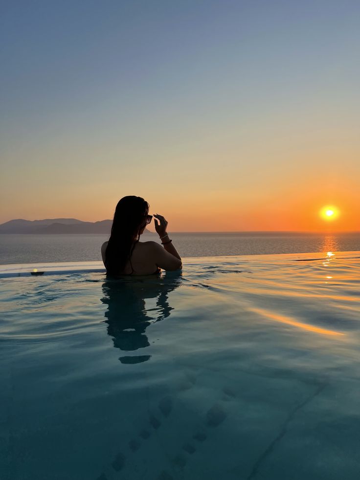 a woman sitting in the middle of a swimming pool with the sun setting behind her