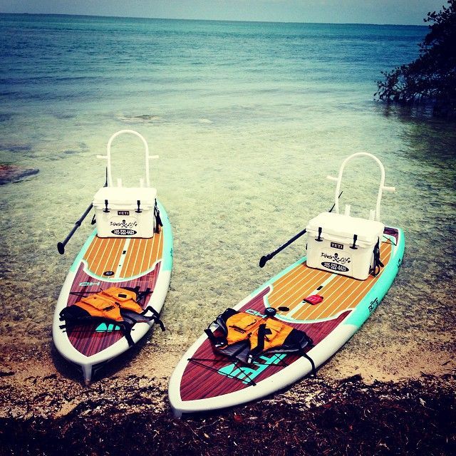 two paddle boards sitting on top of a sandy beach next to the ocean with life vests attached