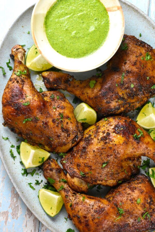 grilled chicken with green sauce and lemon wedges on a white plate next to a small bowl