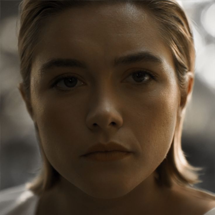 a close up of a person wearing a white shirt and looking at the camera with a serious look on her face