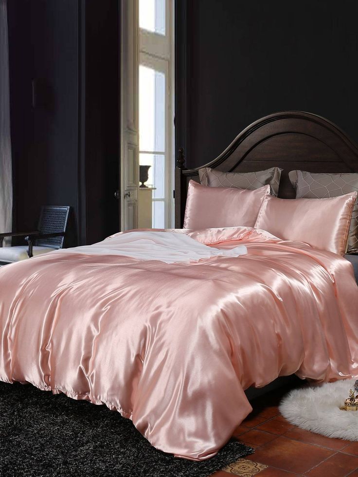 a bed with pink satin sheets and pillows