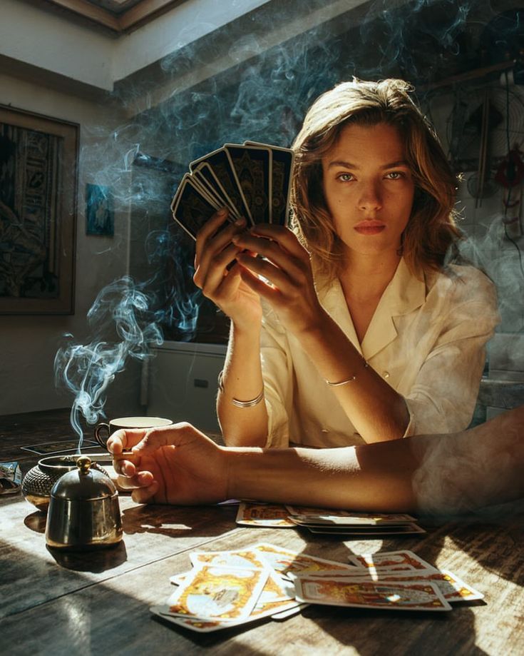 a woman is sitting at a table with cards and a teapot in front of her