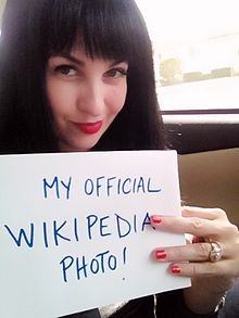 a woman holding up a sign that says, my official wikipedia photo is on it