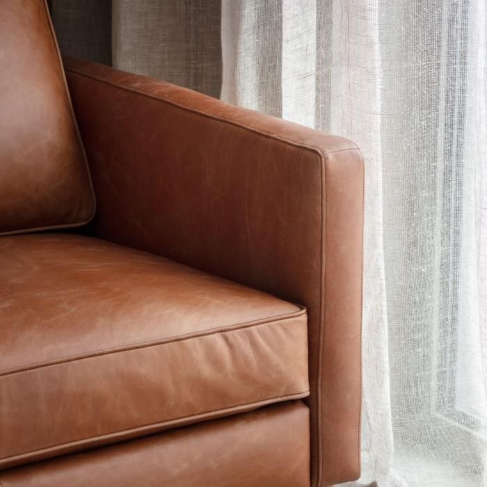 a brown leather couch sitting next to a window