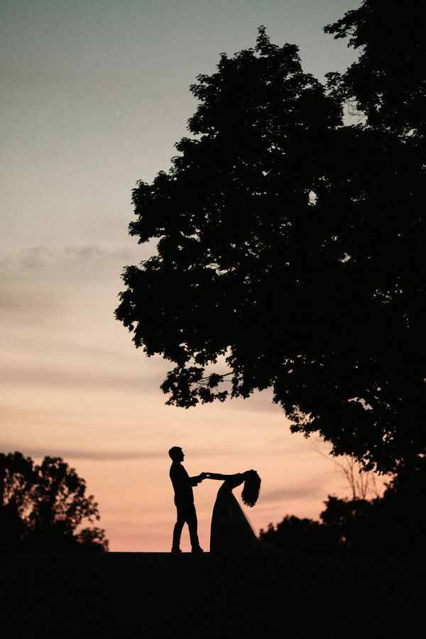 two people standing under a tree at sunset