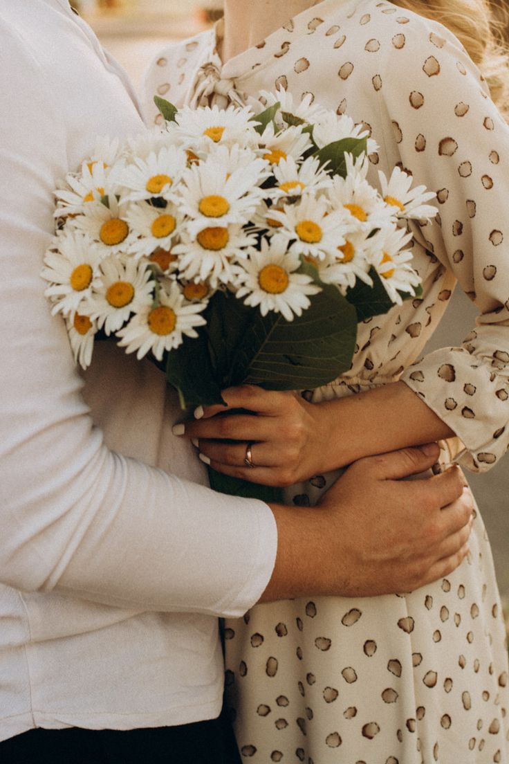 two people are hugging each other and holding daisies in their hands as if they were kissing